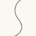 Silver stainless steel ankh pendant with skull motifs on vertical bar and textured ring top, on a box chain necklace.