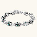 Silver stainless steel skull link bracelet with green crystal eye sockets and engraved detailing, toggle clasp closure.