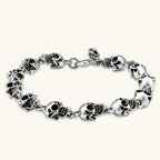 Silver stainless steel bracelet with linked 3D skull charms and a spring-ring clasp, oxidized black detailing, 225mm length.