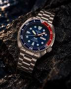 Seiko Prospex PADI Turtle SRPE99 automatic diver's watch on wet dark stone, blue dial and red-blue bezel